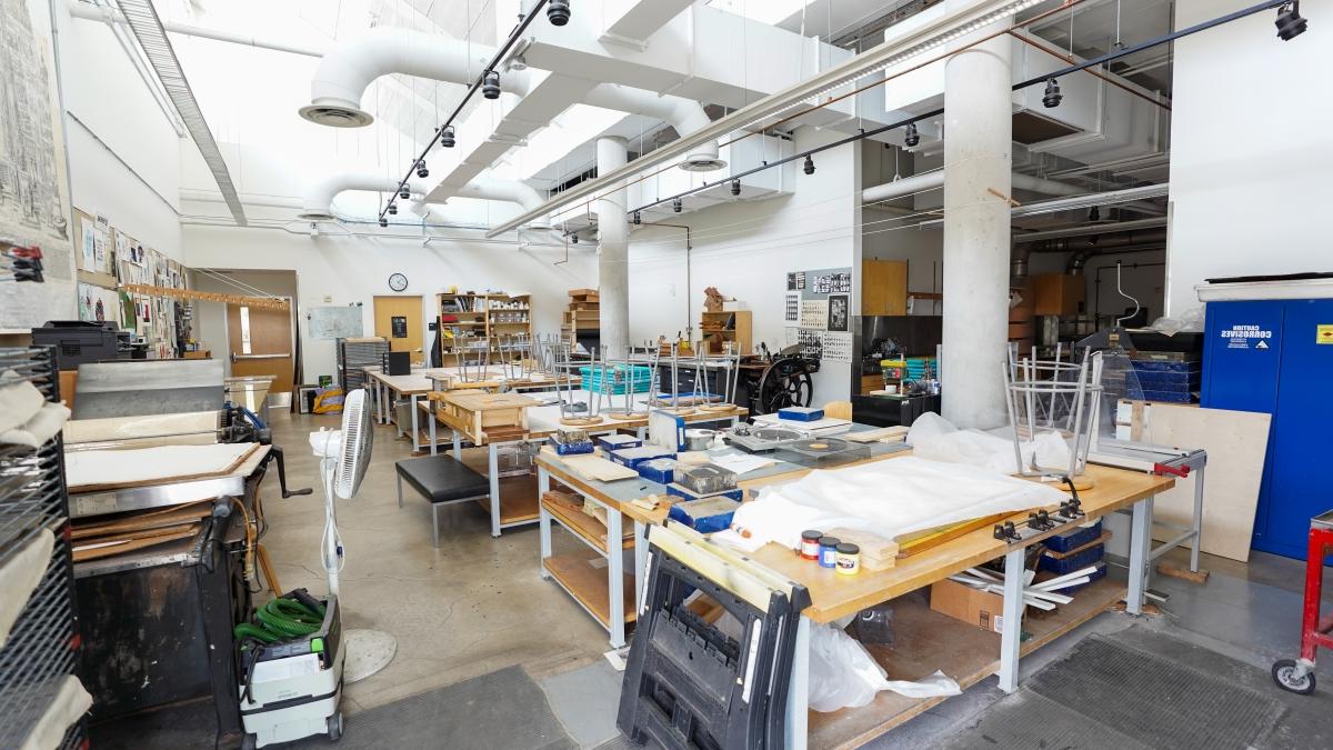 Print making studio filled with tables and stools covered in supplies.